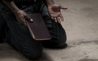 A man kneeling with a Bible